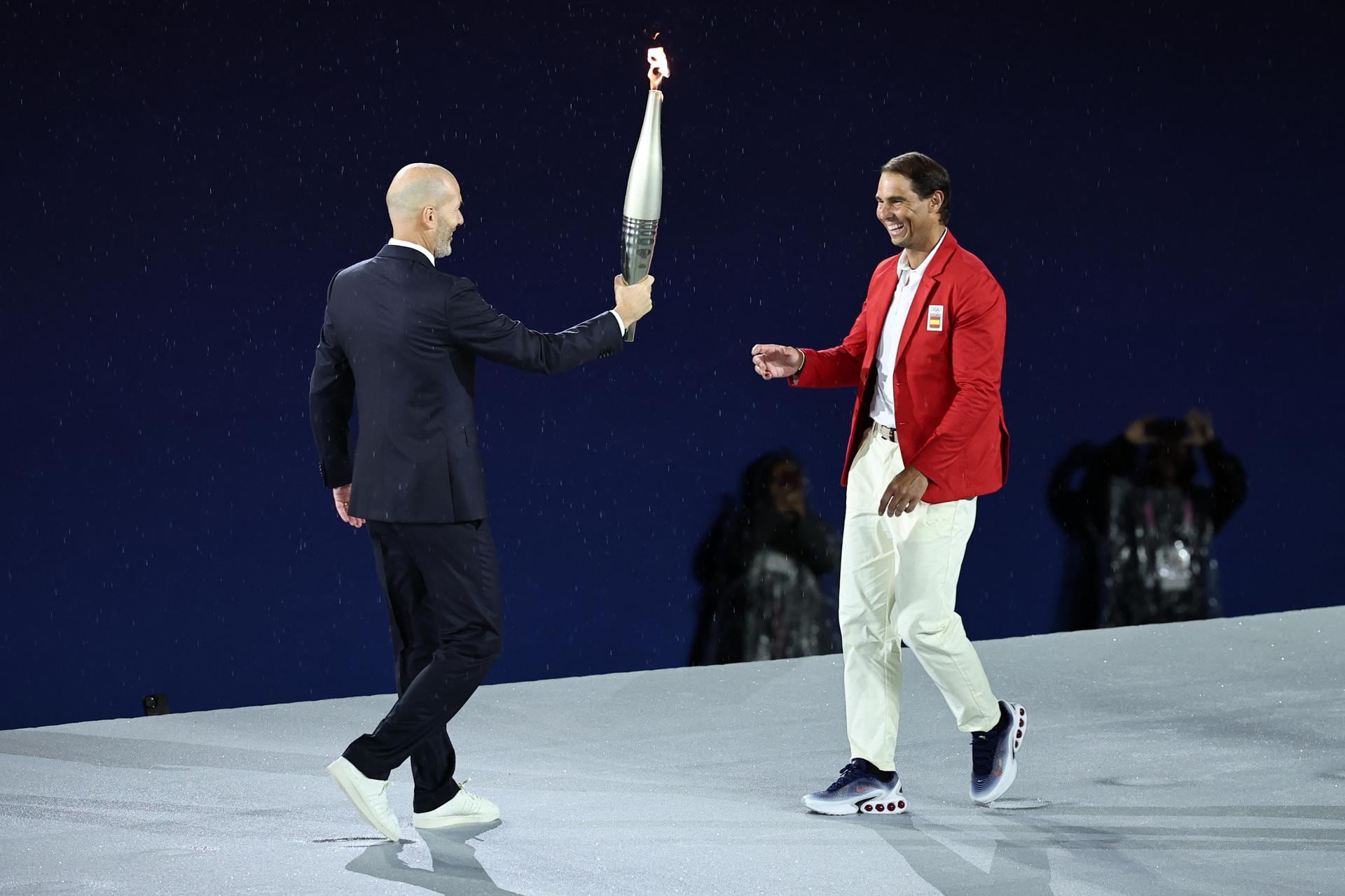 El exfutbolista francés Zinedine Zidane le pasa la llama olímpica al tenista español Rafael Nadal. EFE